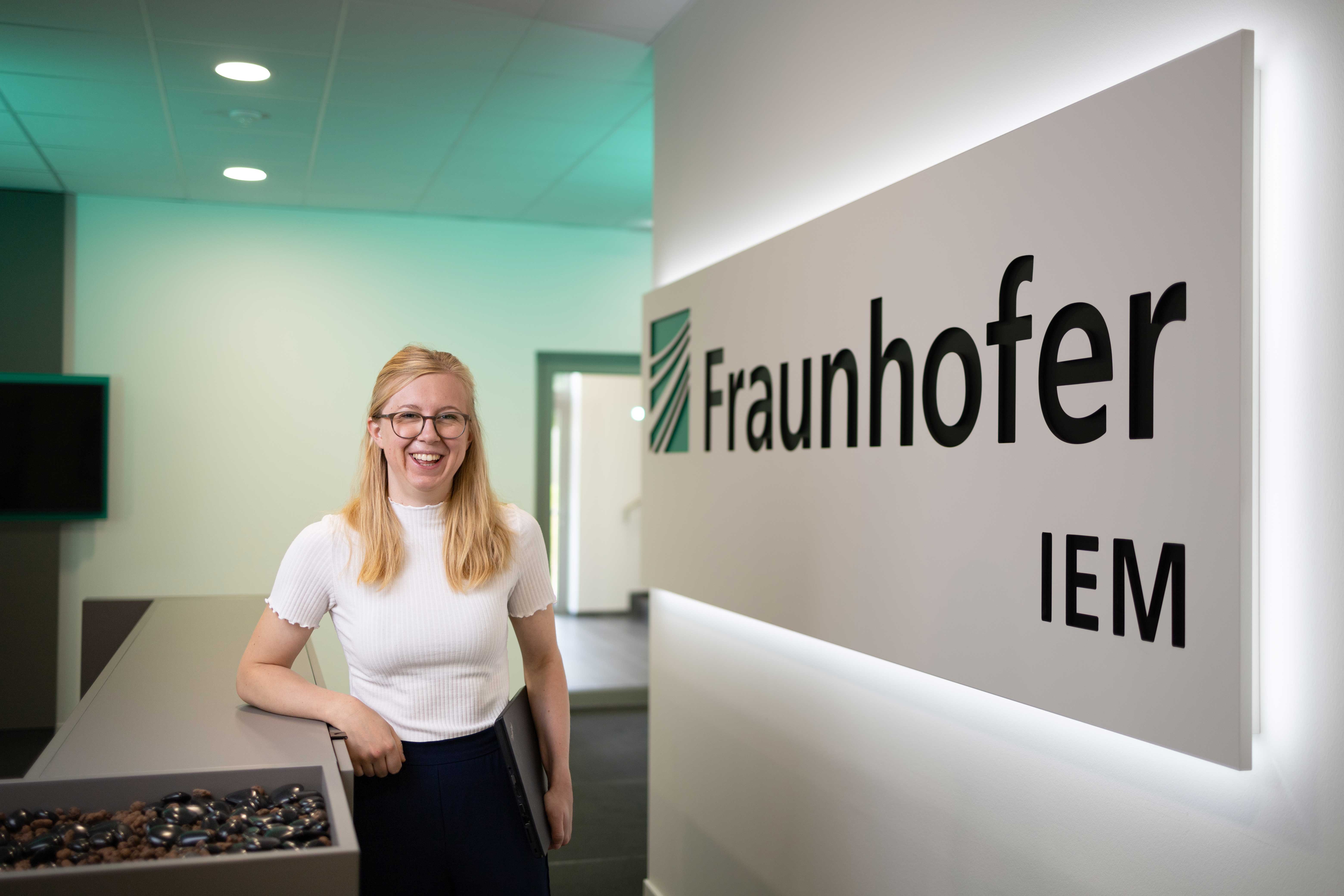 Magdalena Förster vor einem beleuchteten Logo des Fraunhofer IEM.