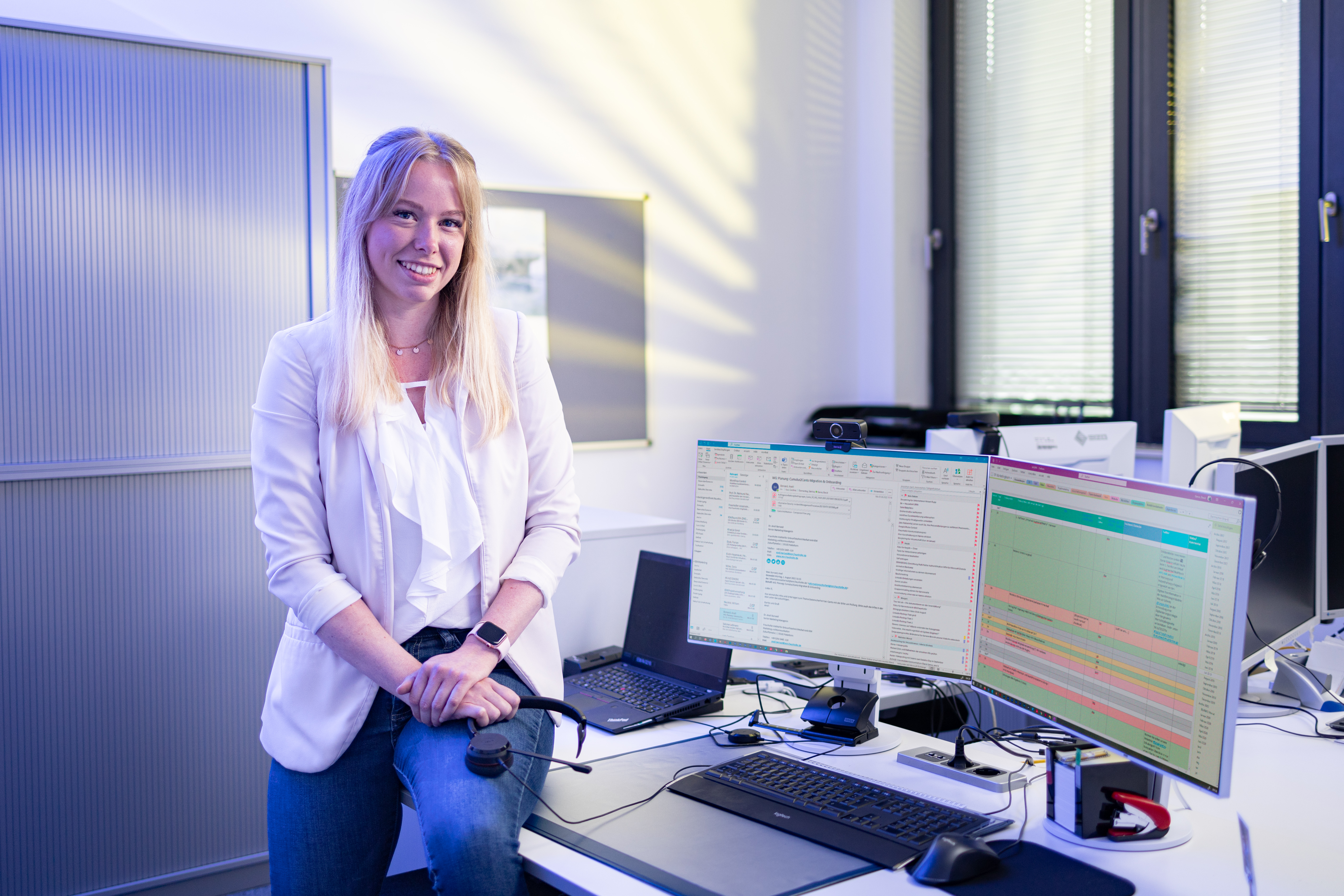 Michelle Ricke Kollmorgen sitzt mit einem Headset in der Hand halb auf einem Bürotisch und lächelt in die Kamera.