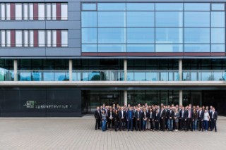 Gruppenfoto mit Frauen und Männern, die nebeneinander und hintereinander vor dem Gebäude Zukunftsmeile 1 stehen.