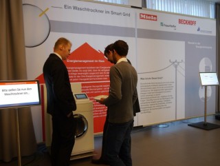 Drei Männer vor einem Waschtrockner an einer Messewand