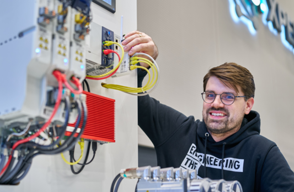 News Effizientere Softwareupdates Industriesteuerung Mitarbeiter steht vor Anlage und präsentiert eine automatisierte Lösung.