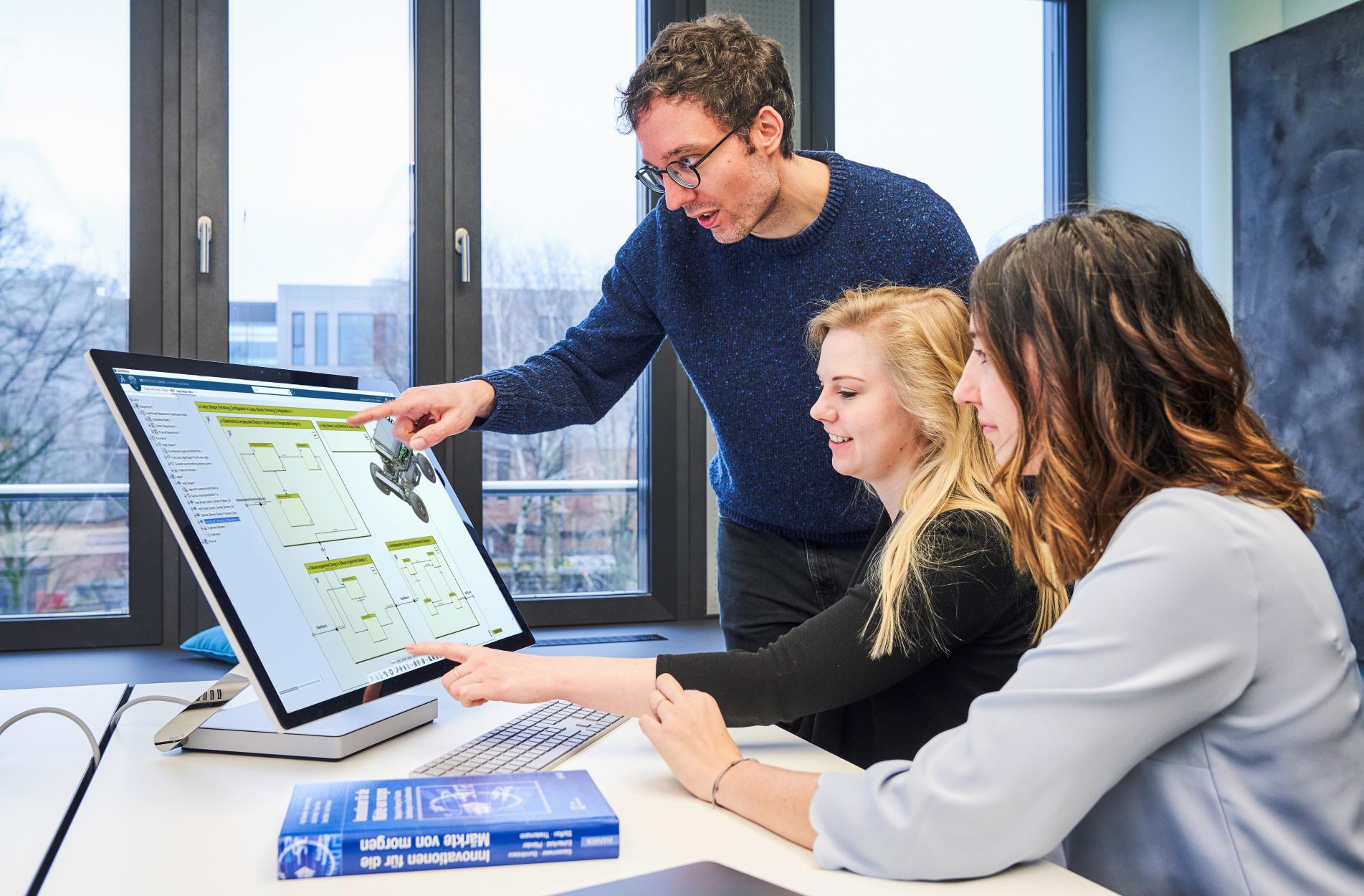 News Dassault Systemes Drei Personen sitzen vor einem Bildschirm und unterhalten sich.