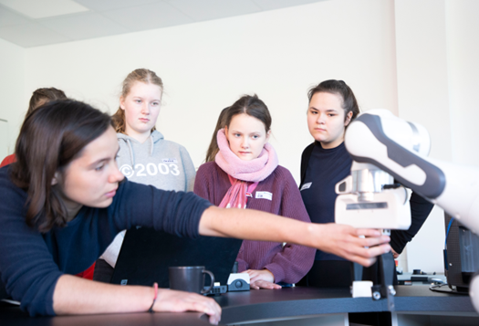 Gruppe von Mädchen steht an Roboterarm.