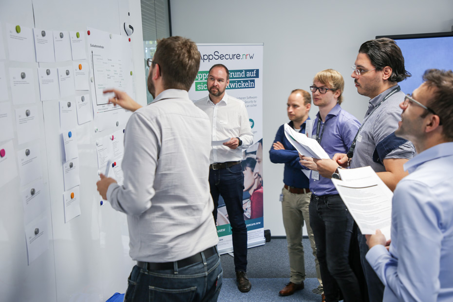 News AppSecure.nrw Projektabschluss Studie Ein Mann erklärt einer Gruppe von 5 Personen einen Sachverhalt an einem Whiteboard.