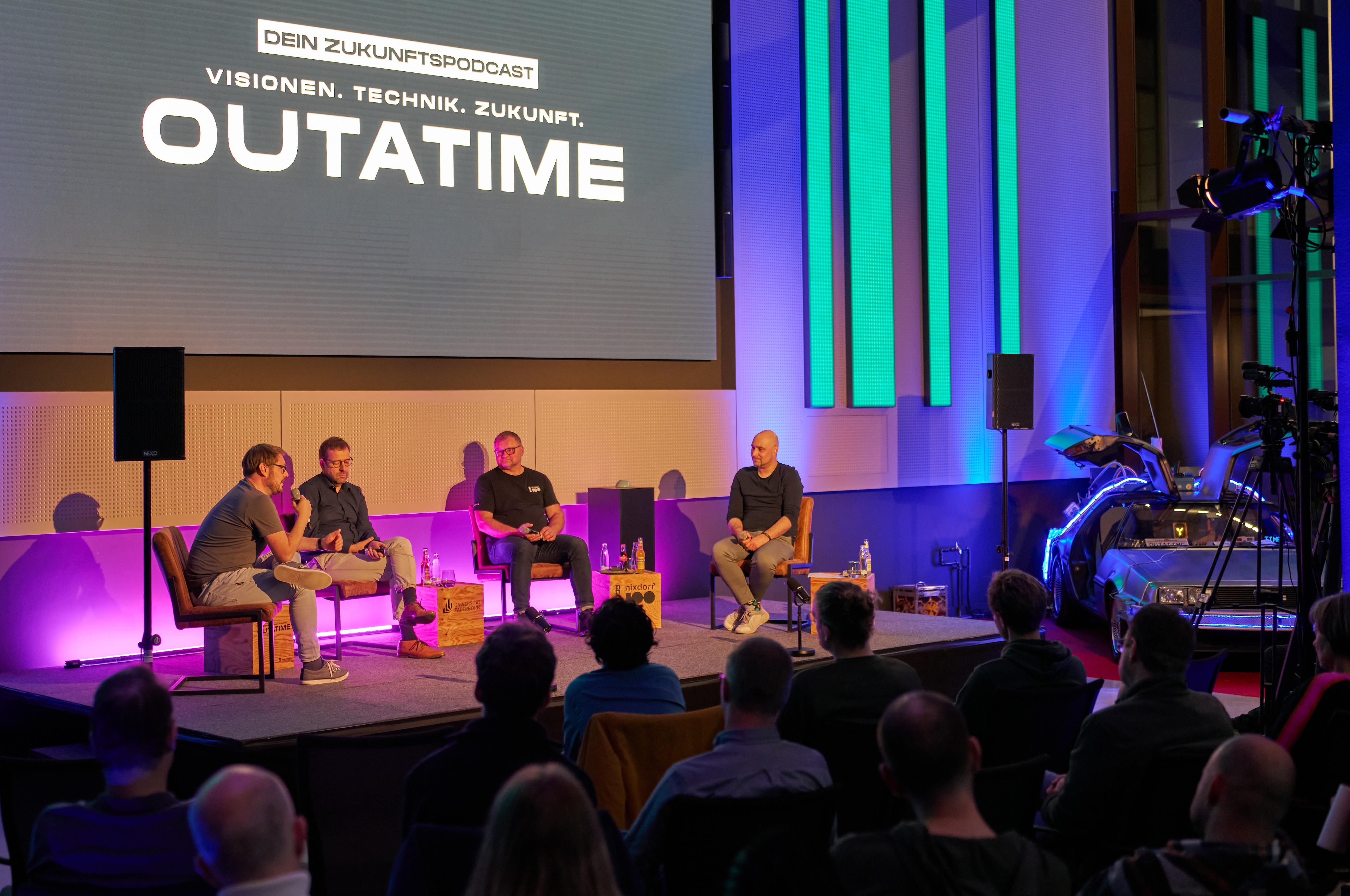 Podcaster sitzen auf der Bühne und erzählen dem Publikum etwas.