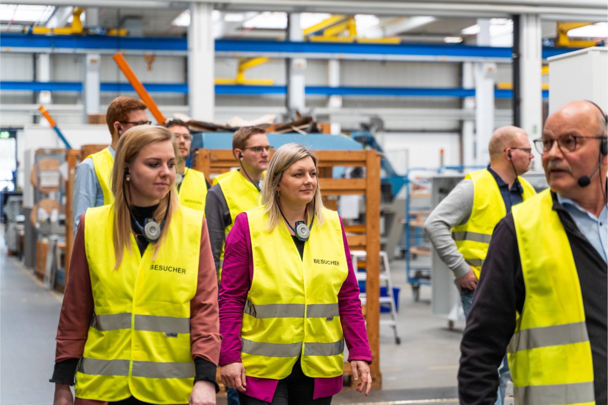 Sieben Menschen laufen mit gelben Westen durch eine Halle