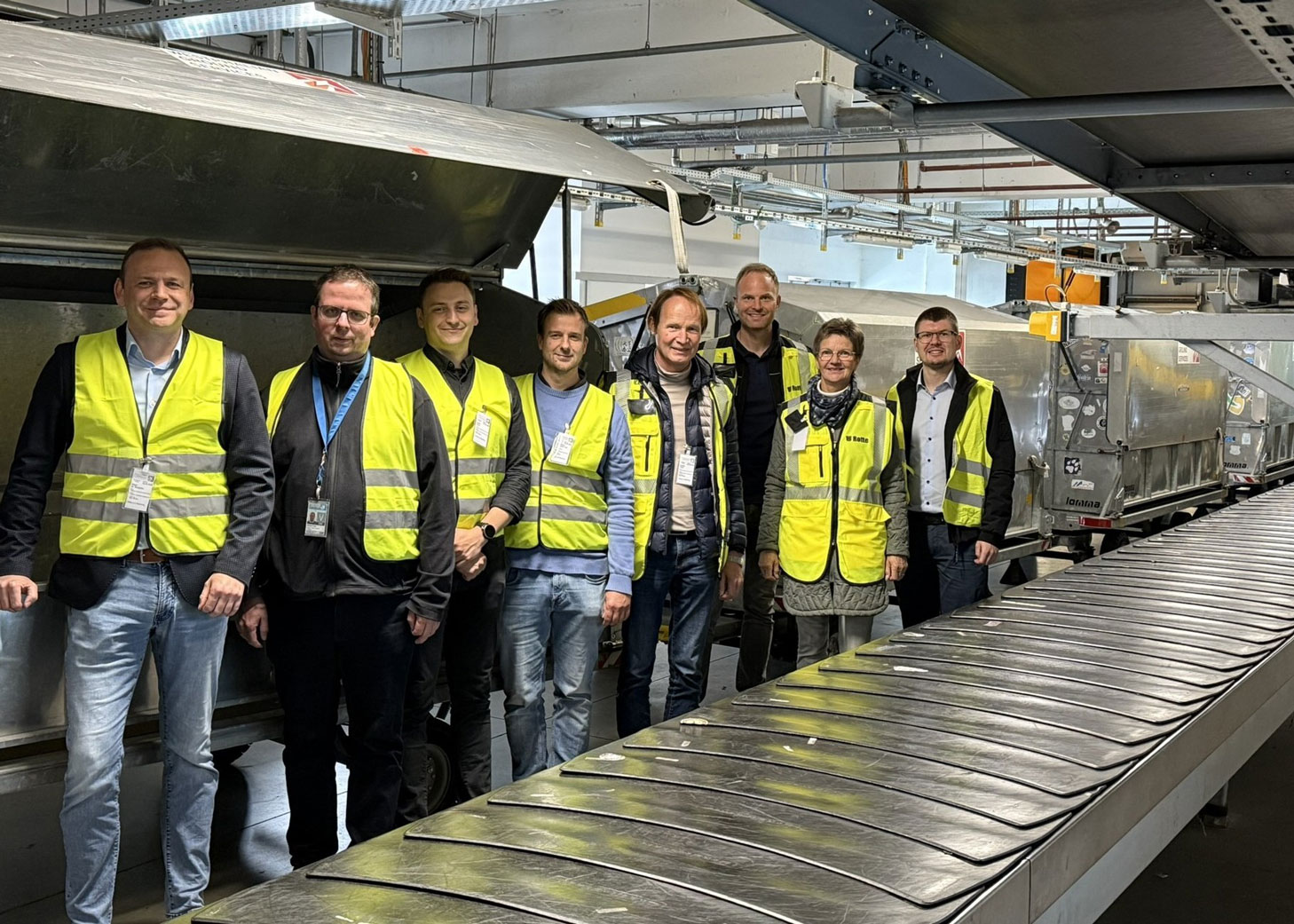 Projektstart AG für NBA Gruppenbild der Mitarbeiter vor einem Gepäckband stehend.