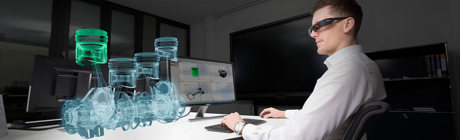Mann mit AR-Brille an einem Monitor schaut auf ein virtuelles Objekt.