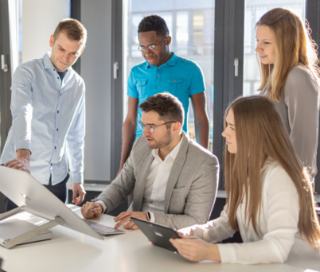 Gruppe sitz gemeinsam vor Bildschirm und hört Erklärung eines Kollegen zu.