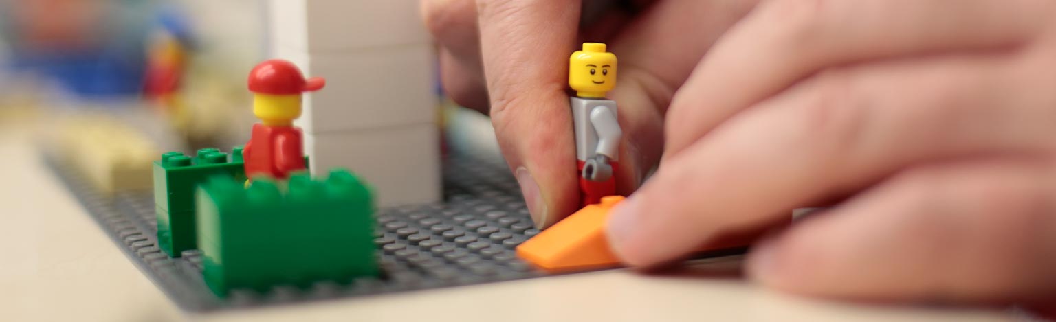 Detailansicht von zwei Händen, die eine Spielfigur auf ein Modell aus Spielsteinen setzen.