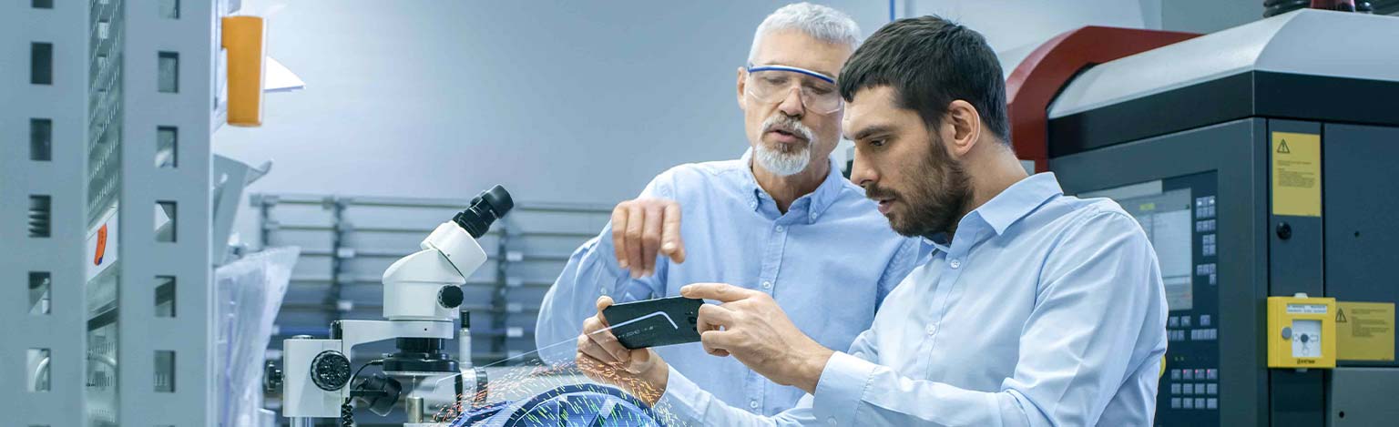 Zwei Männer in einer Industrie-Halle. Einer Hält ein Smartphone in der Hand und beide schauen auf ein virtuelles Objekt.