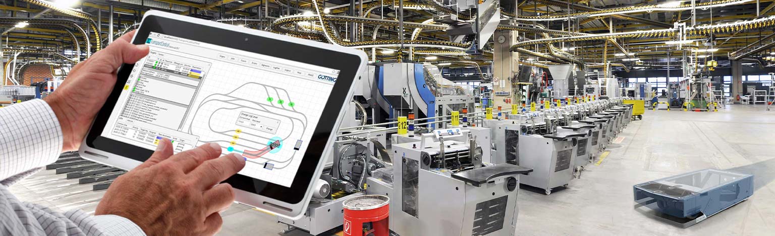 Zwei Hände halten ein Tablet in einer Industriehalle. Auf dem Bilschirm ist ein Navigationsplan für Systeme in der Halle zu sehen.