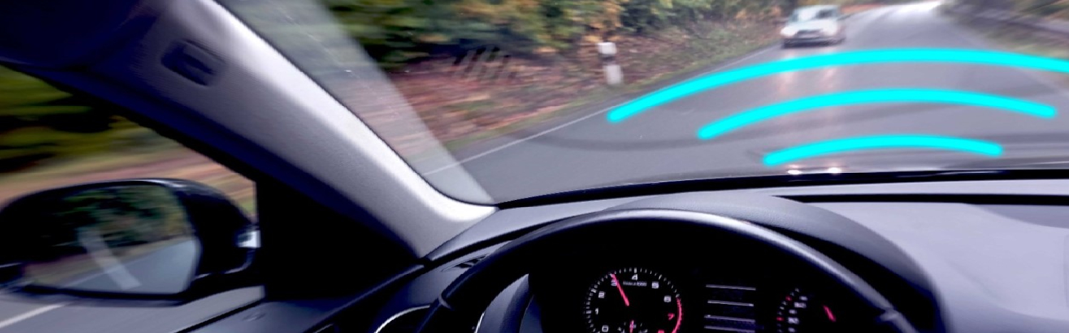 Fahrerblick über das Armaturenbrett auf die Straße, auf welcher ein entgegenkommendes KFZ mittels blauer Sensorgrafik erfasst wird.