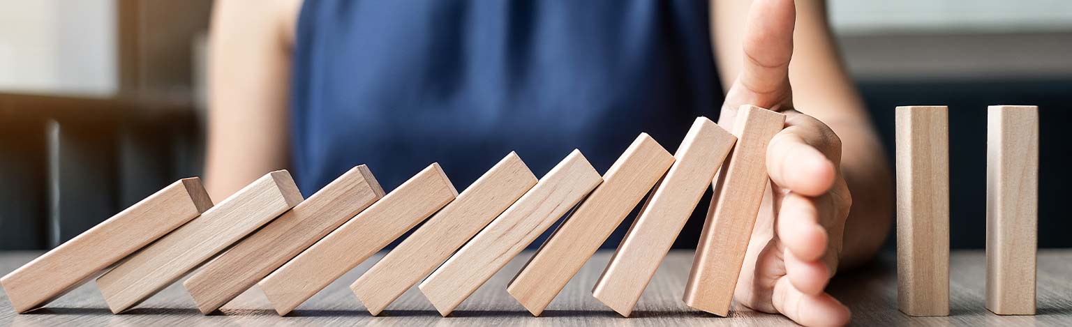 Eine Hand, welche Dominosteine aus Holz umstößt.