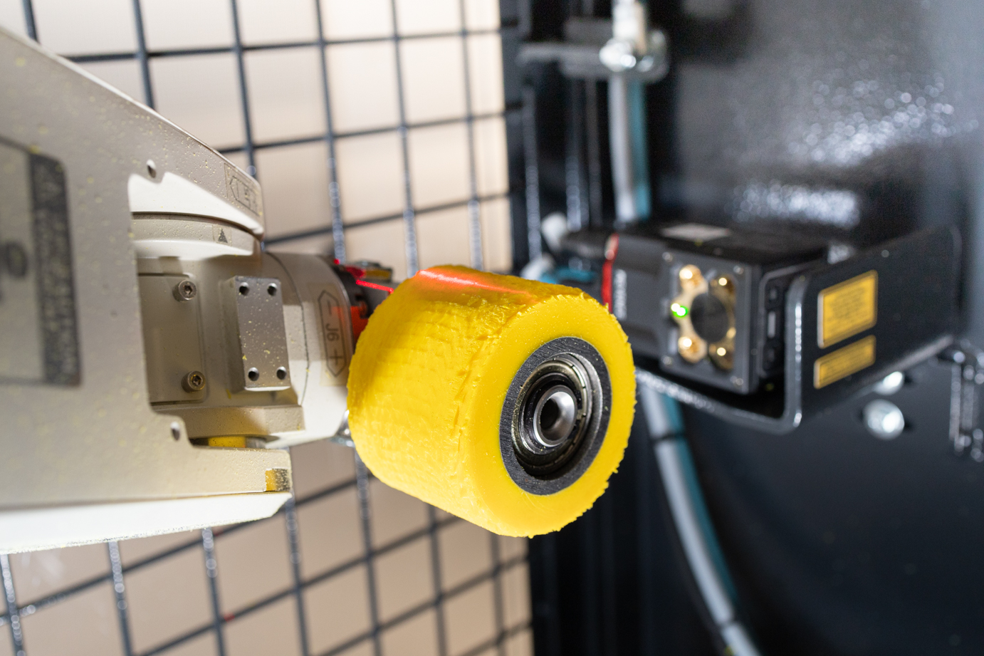 Der Roboterarm des RoboGrinders hält eine gelbe Gummirolle vor einen Scanner, welcher diese identifiziert.