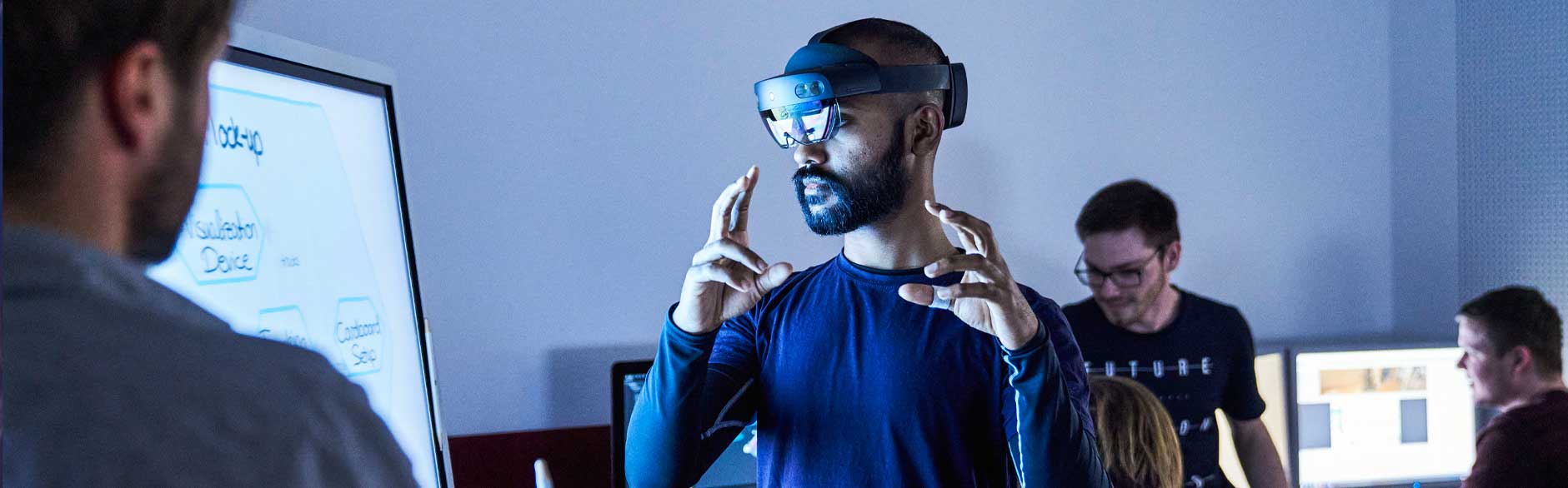 Mann mit AR-Brille an einem Monitor greift ein virtuelles Objekt.