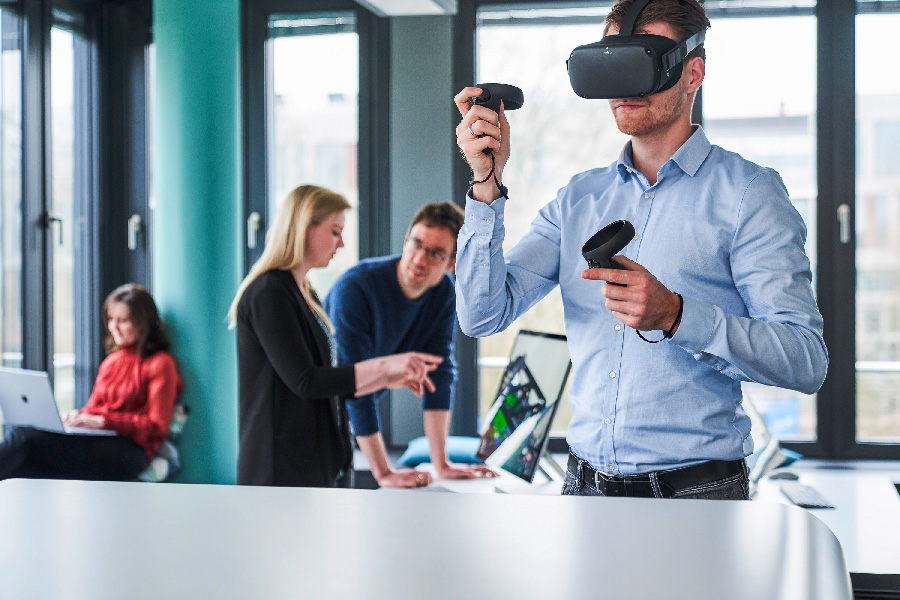 Im SE Live Lab verwendet ein Mann eine VR Brille, eine Frau arbeitet an ihrem Laptop und zwei weitere Personen  diskutieren vor einem Computer.