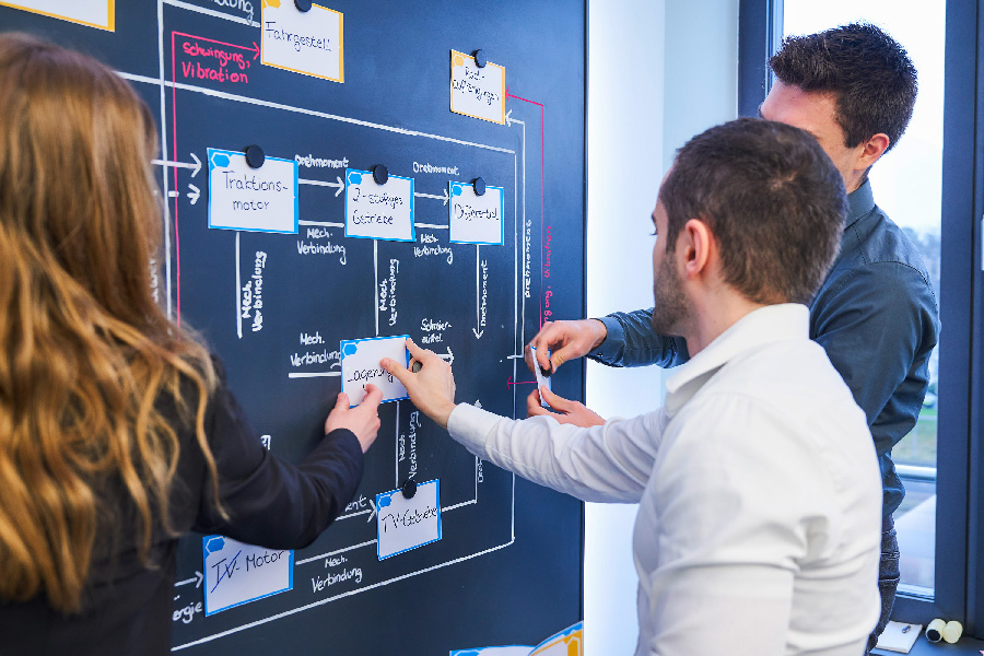 A group of three people works in the SE Live Lab and discusses in front of a blackboard.