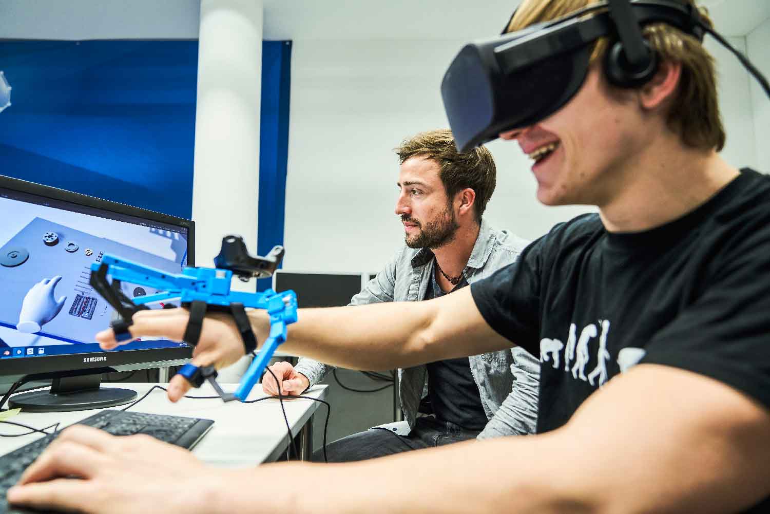 Zwei Männer sitzen im AR VR Lab und testen einen VR-Handsschuh.
